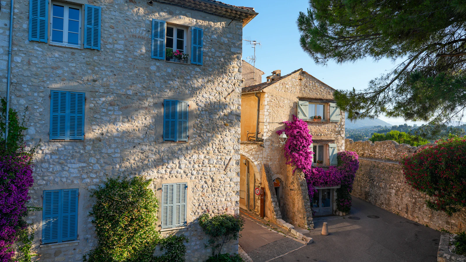 Maisons en pierre aux volets bleus et fleurs violettes en façade
