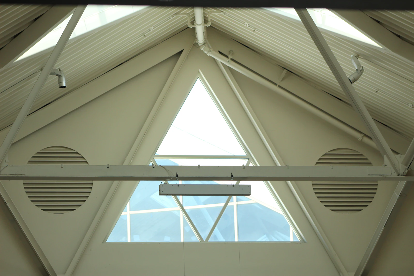 Plafond blanc percé de grilles de ventilation circulaires autour d'une fenêtre triangulaire