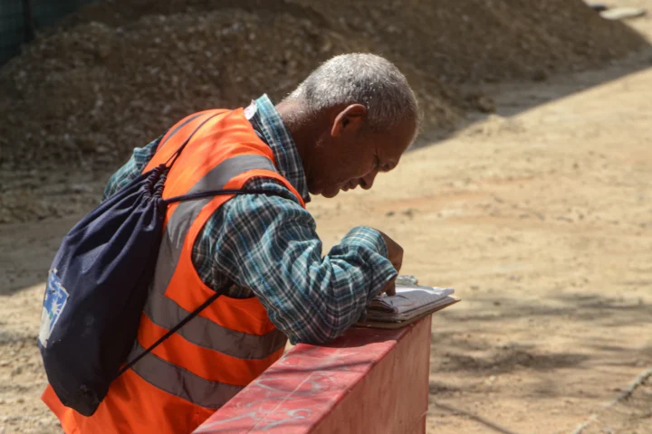 Homme en gilet orange prenant des notes sur une feuille en extérieur