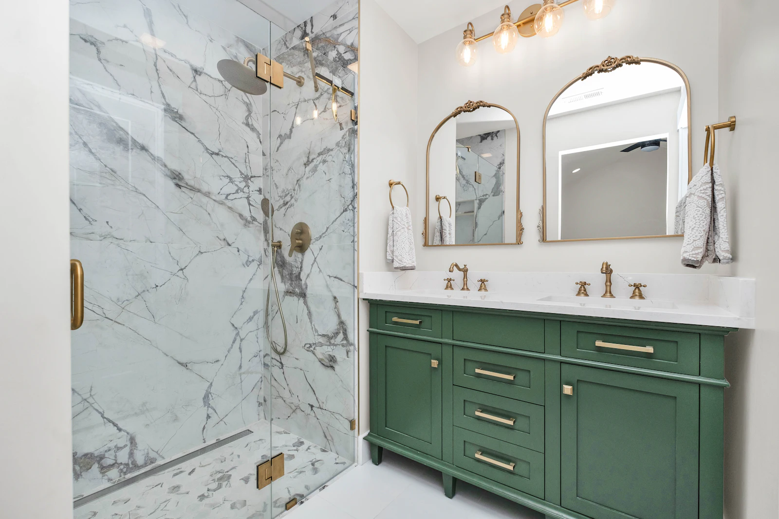 Salle de bain rénovée avec douche vitrée en marbre et meubles verts